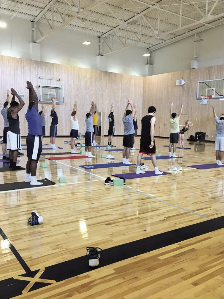 The men's basketball team is guided through a yoga flow, a series of poses that synthesize for a unified purpose in the body