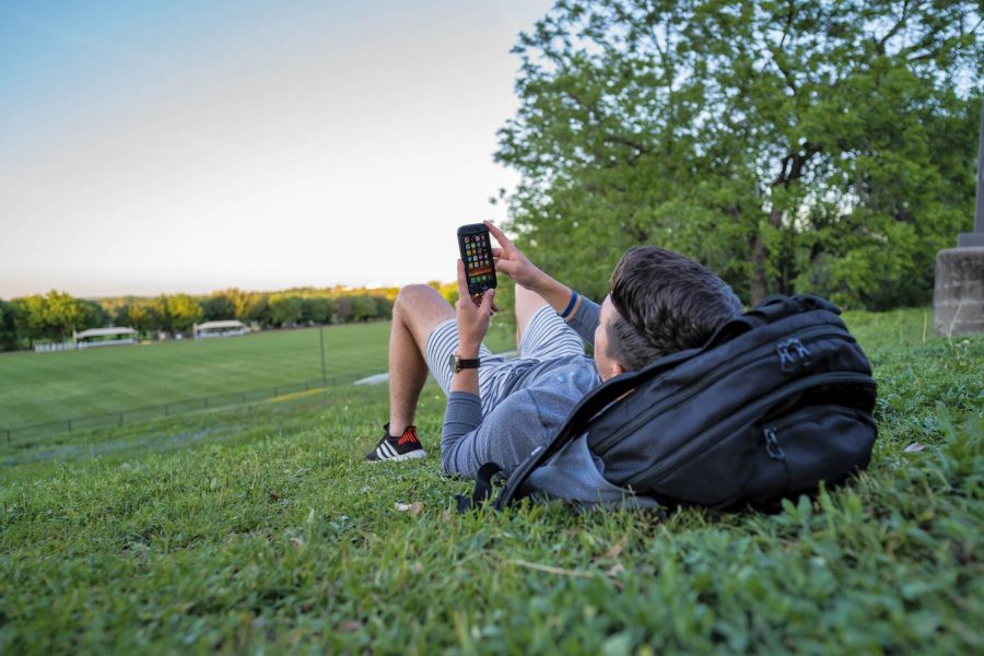 St. Edward’s student lounges with his phone by the soccer field. 