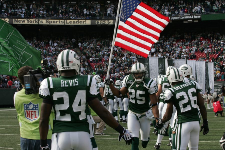 Kerry Rhodes of the New York Jets carries an American Flag on to the field during pre-game introductions in 2009. The issue of mandatory patriotism and playing the national anthem before games has become a hotly discussed topic in recent years.