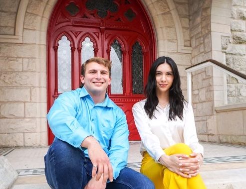 Ochoa and Garrets pose in front of the red doors of Main Building. 