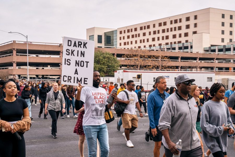Marchers continue down their journey. One advocate walks with a sign and sporting a t-shirt that reads "Defend Black Lives."