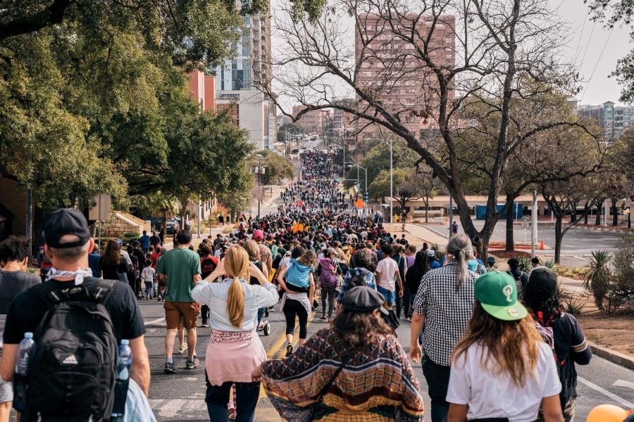 People march down East 11th Street toward Huston-Tillotson University, spanning from sidewalk to sidewalk. 