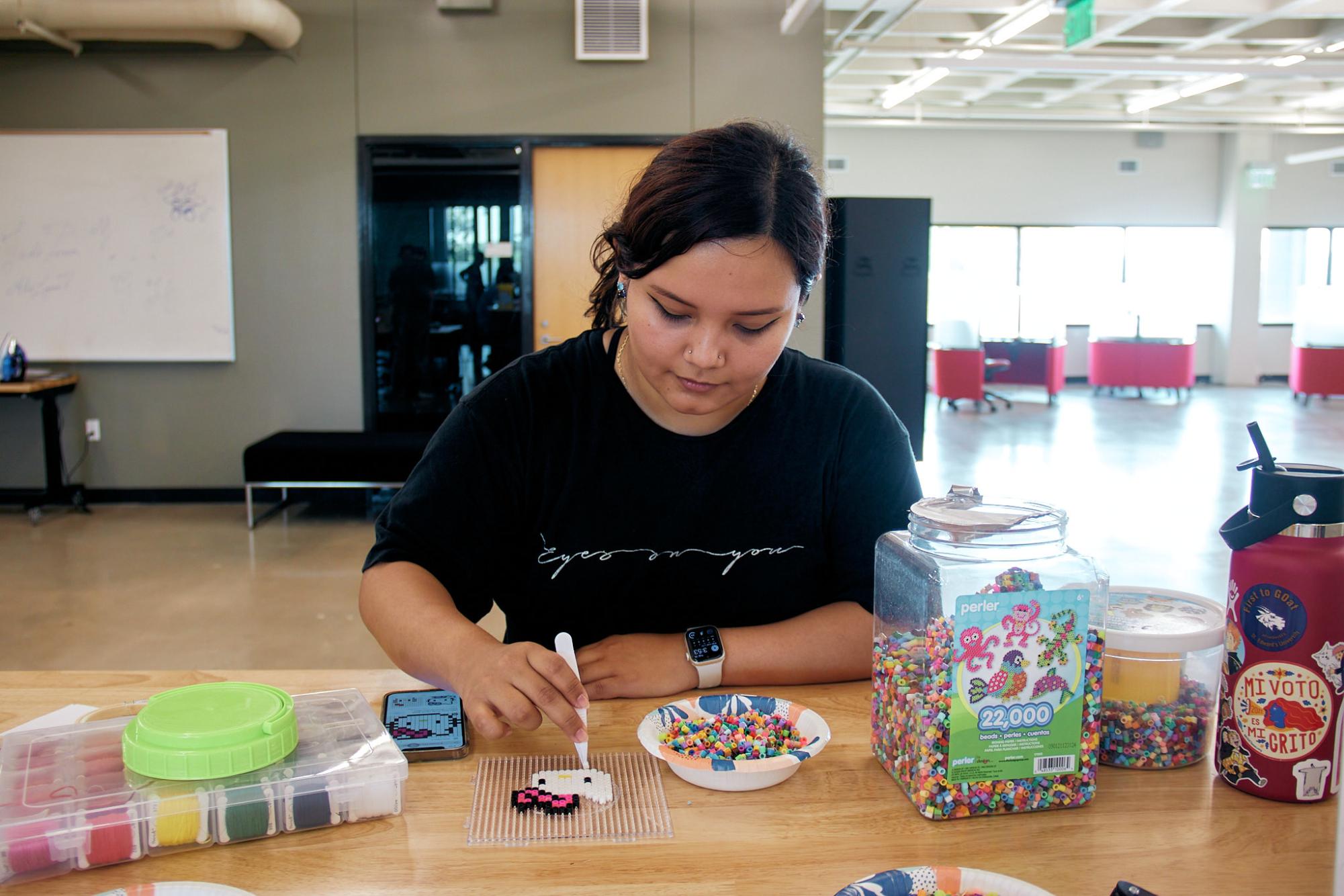 Library aid Patricia Martinez demonstrates pixel art by creating a Hello Kitty made of perler beads.