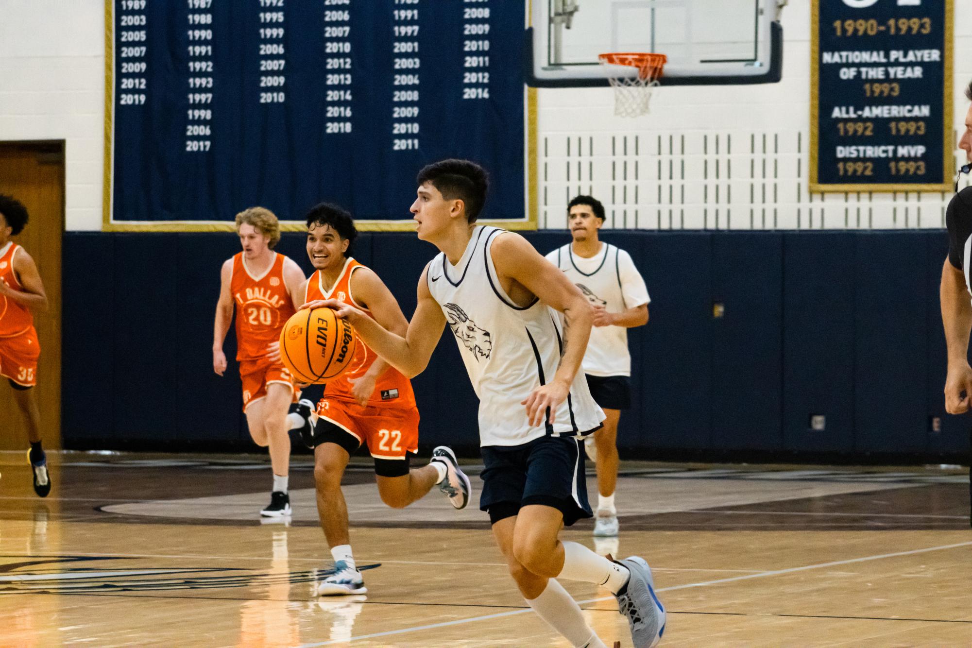SEU mens basketball player Gavino Ramos travels the court with possession of the ball. UT Dallas Comets players scramble to apply defense.