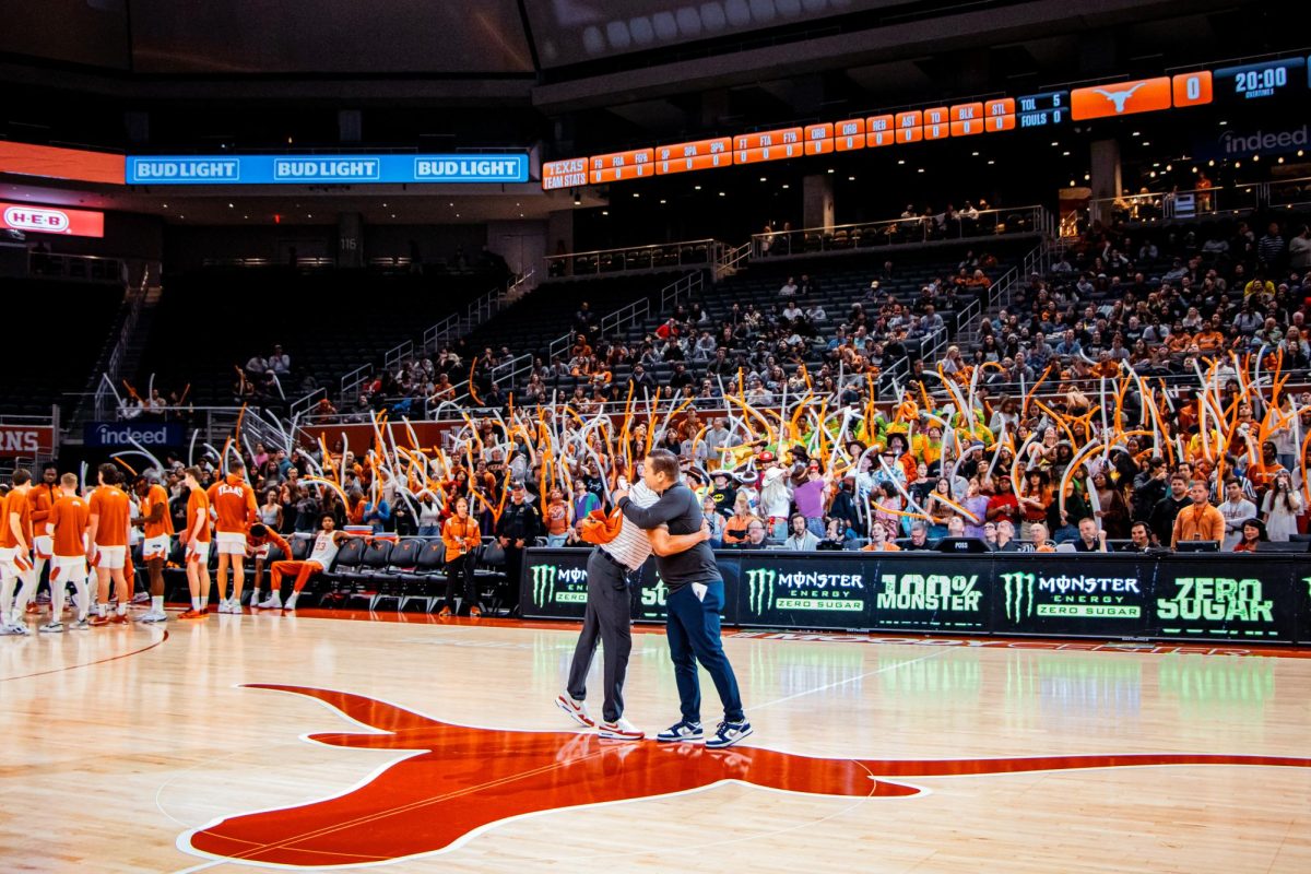 Head coaches Rodney Terry (left) and Andre Cook (right) hug prior to the game after exchanging jerseys as the crowd cheers them on.