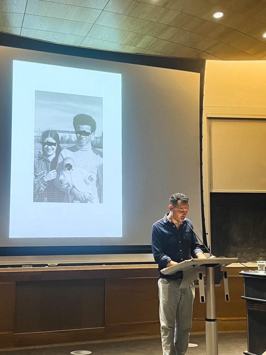 Daniel Torres in Carter Auditorium, reading portions from Blackouts. He stands in front of a screen, projecting an image.