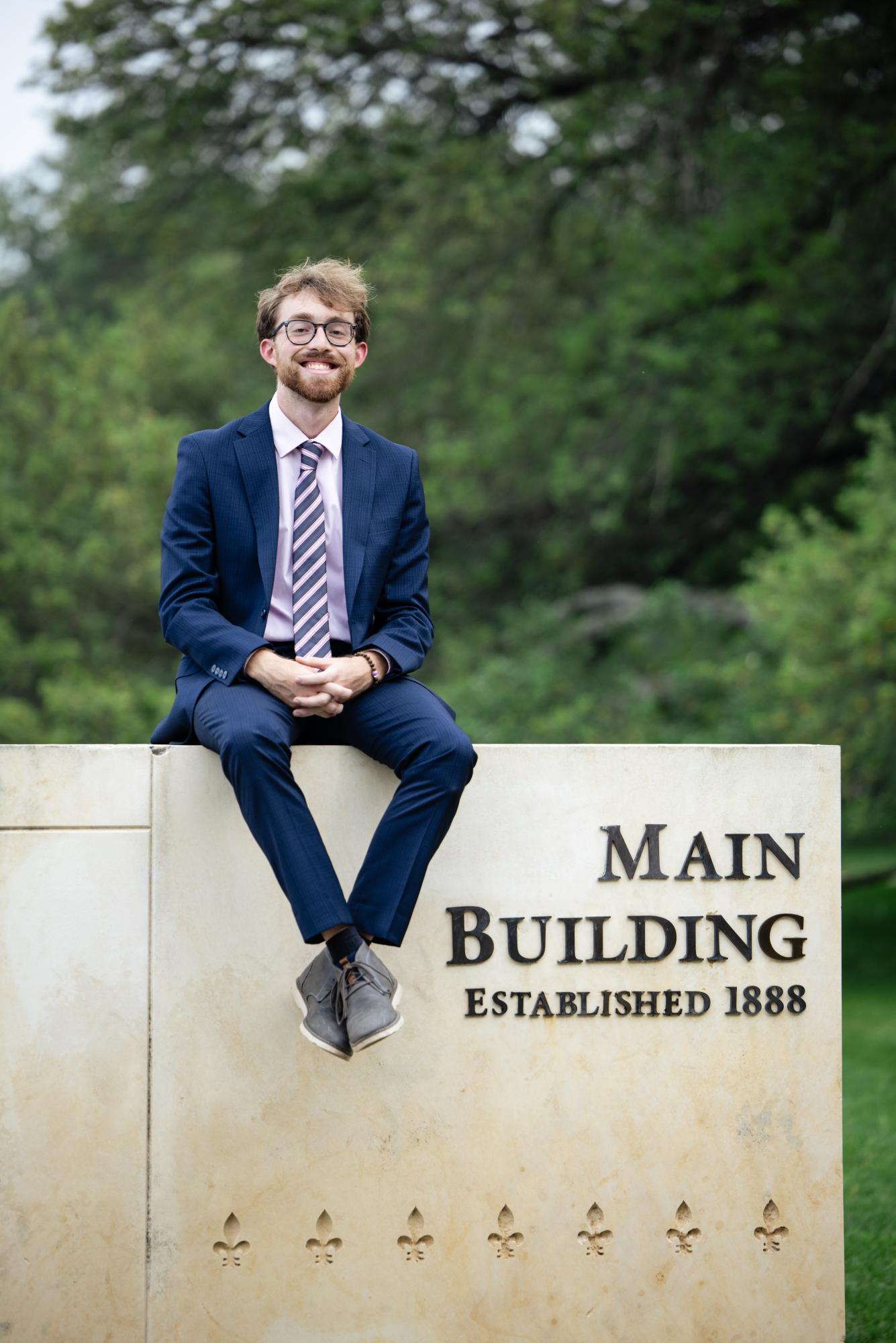 Max Hoelker sits on Main Building sign on his final days on the Hilltop.